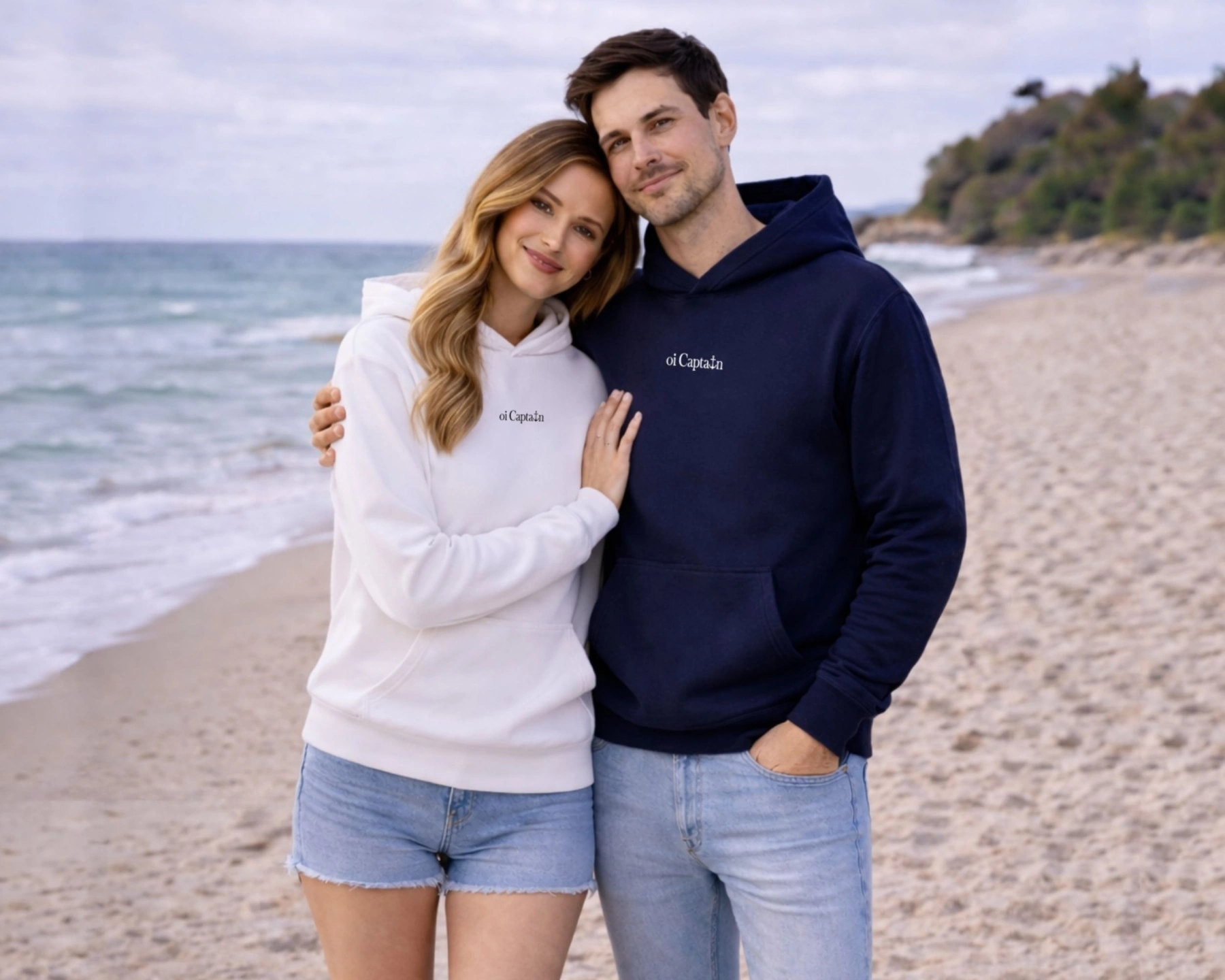 female model wearing oi captain seas the day hooded sweatshirt in white and male model wearing oi captain seas the day hooded sweatshirt in navy front poses coastal lifestyle.jpg